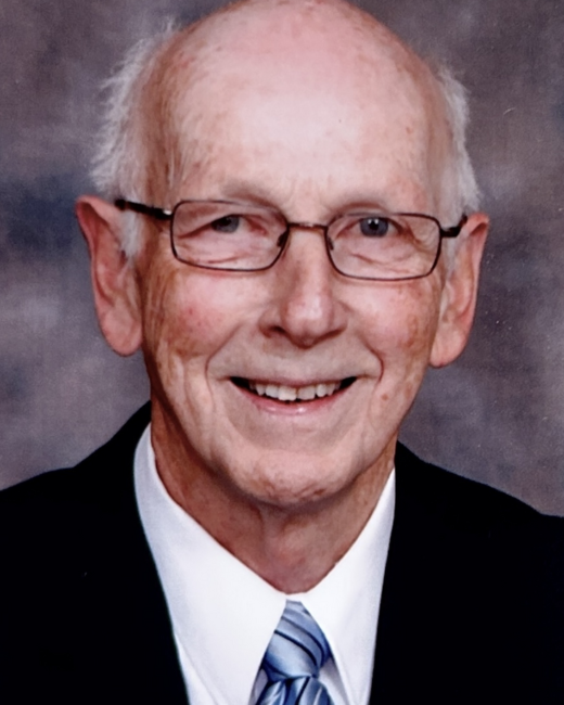 Elderly man in glasses smiling in suit and tie.