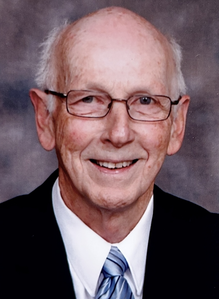 Elderly man in glasses smiling in suit and tie.