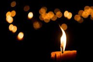 Candle glowing with blurred lights in background.