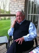 Elderly man sitting outdoors on a porch chair.