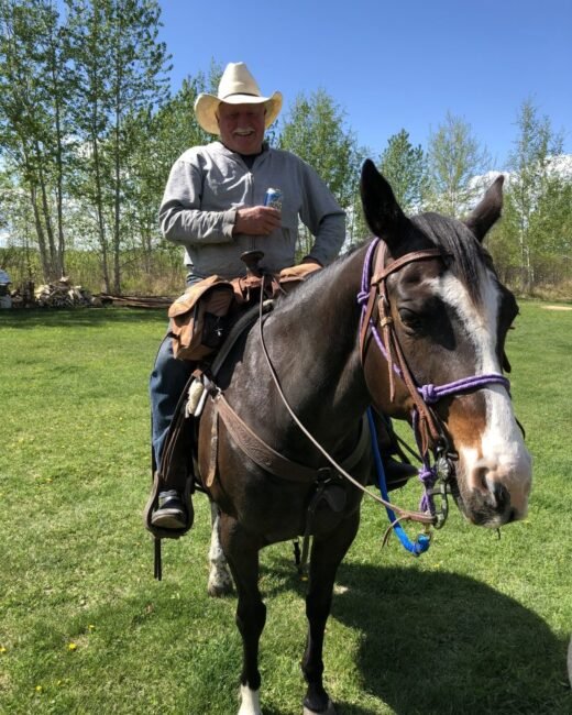 Smiling man on horse holding a can outside.