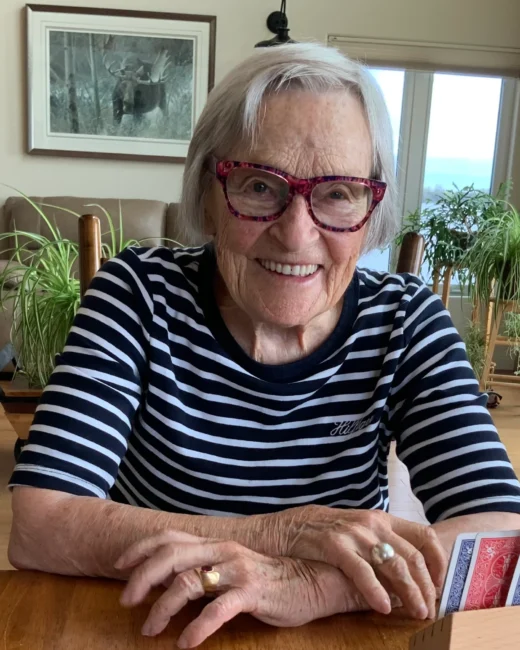Smiling elderly woman with glasses plays cards at home.
