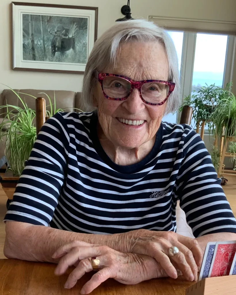 Smiling elderly woman with glasses plays cards at home.