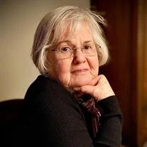 Elderly woman with gray hair sitting indoors.
