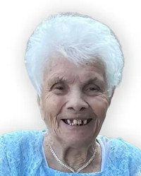 Smiling elderly woman with white hair and blue shirt.