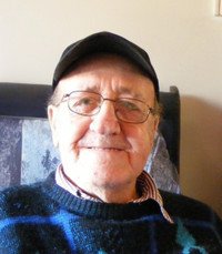 Elderly man smiling wearing a black cap indoors.