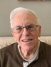 Smiling elderly man with glasses on sofa.