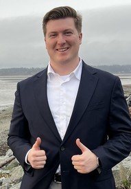 Smiling man giving thumbs up near beach.