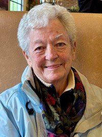 Smiling elderly woman in a blue jacket indoors.