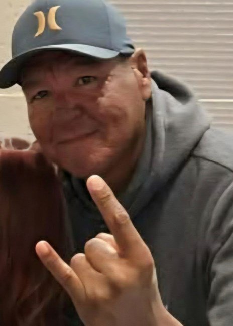 Person smiling wearing cap and making hand gesture.