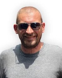 Smiling person wearing sunglasses and a gray shirt.