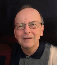 Smiling person wearing glasses against dark background.
