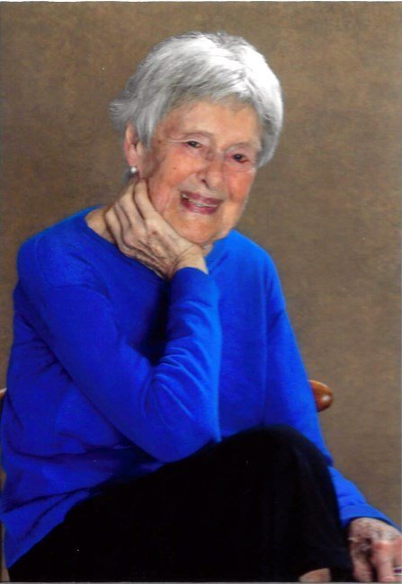 Smiling elderly woman in blue sweater, seated pose.