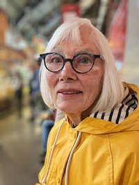 Elderly woman in yellow jacket indoors.