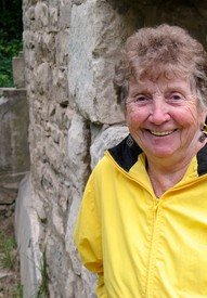 Smiling person in yellow jacket near stone wall.