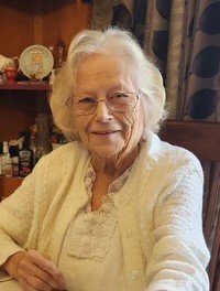 Elderly woman smiling, wearing a white sweater indoors.