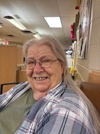 Smiling elderly woman with long gray hair indoors.