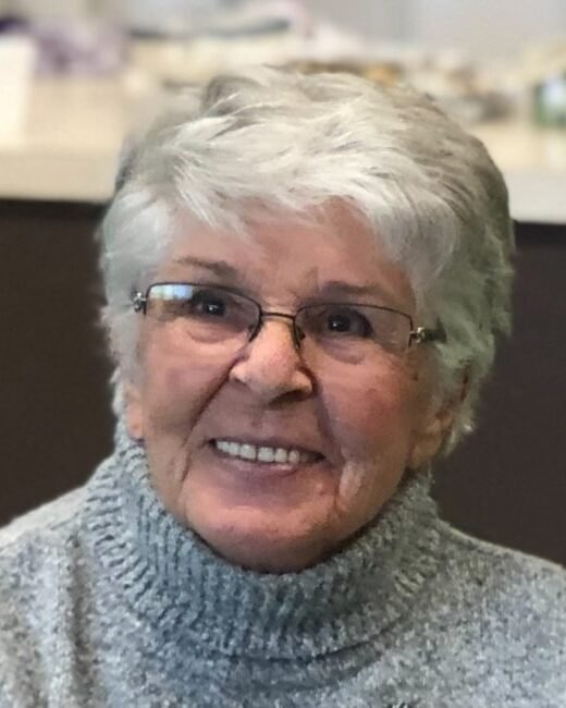 Smiling elderly woman wearing glasses and gray sweater.