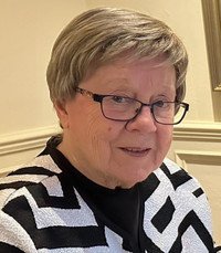 Elderly woman with glasses, short hair and patterned sweater.