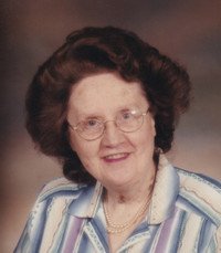 Elderly woman smiling in glasses and striped shirt.