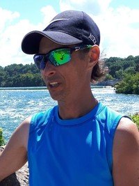 Person by river wearing sunglasses and cap.