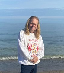 Person in sweater smiling by the ocean.