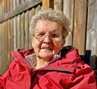 Elderly woman in red jacket outdoors smiling.