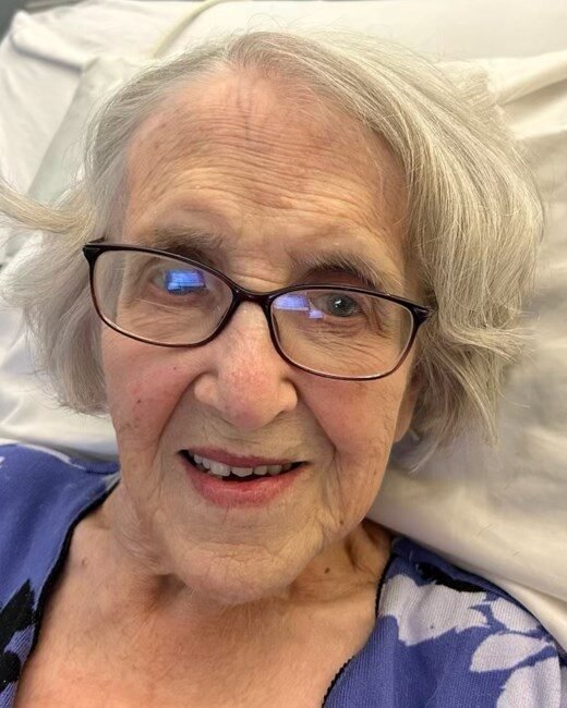 Smiling elderly woman with glasses in hospital bed.