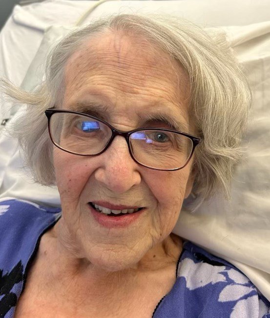 Smiling elderly woman with glasses in hospital bed.