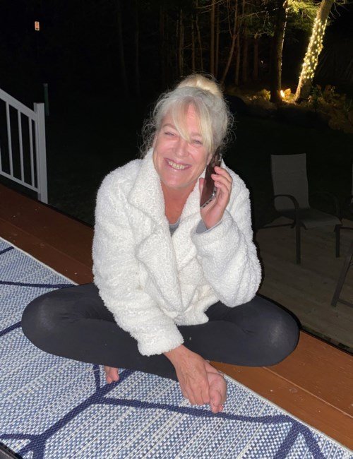 Woman smiling, sitting cross-legged on deck at night.