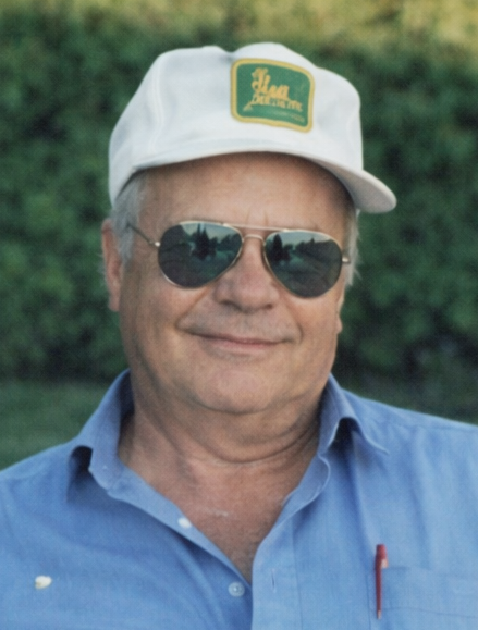 Smiling man in sunglasses and white cap outdoors.