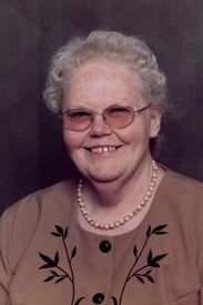 Smiling elderly woman in glasses and pearl necklace.