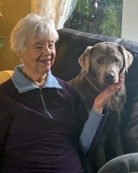 Elderly woman smiling with large gray dog on couch.
