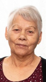 Elderly woman with short gray hair, wearing polka dot blouse.