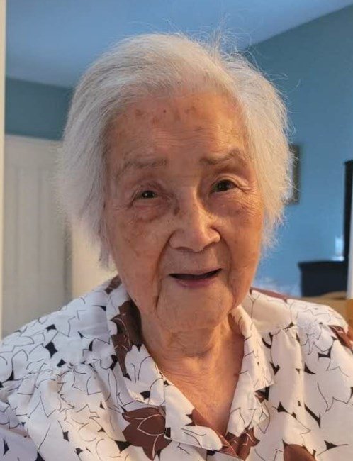 Elderly woman smiling indoors with white hair.