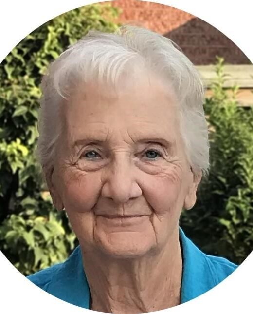 Elderly woman smiling outdoors with greenery background.