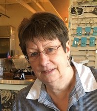 Person in cafe with glasses and short hair.