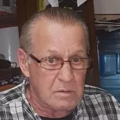Older man with glasses and plaid shirt indoors.