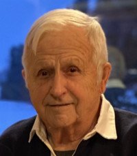 Elderly man smiling indoors with sweater.