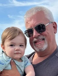 Man and child smiling outdoors under blue sky.