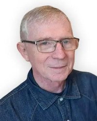 Elderly man with glasses and denim shirt.