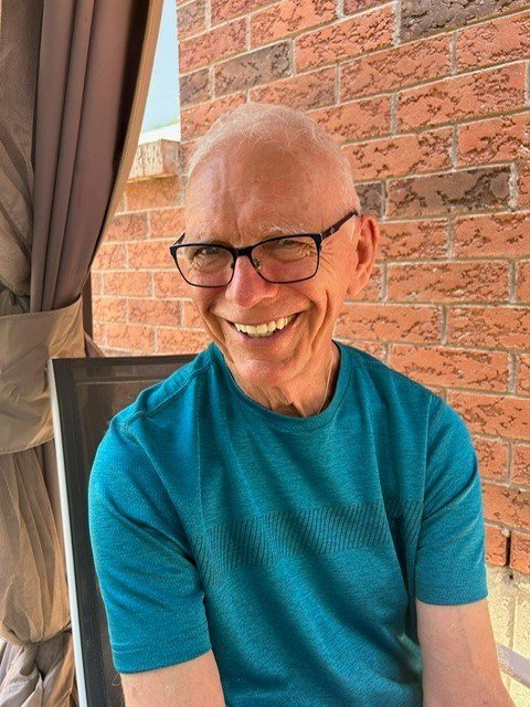 Man smiling outdoors in a teal shirt.