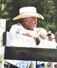 Older man in cowboy hat on wooden fence.