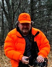 Hunter in orange jacket holding antlers in forest.