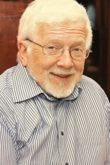 Smiling older man with glasses and striped shirt.
