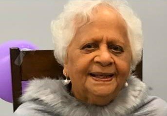 Smiling elderly woman with purple balloon background.