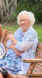 Elderly woman in floral dress sitting on a bench.