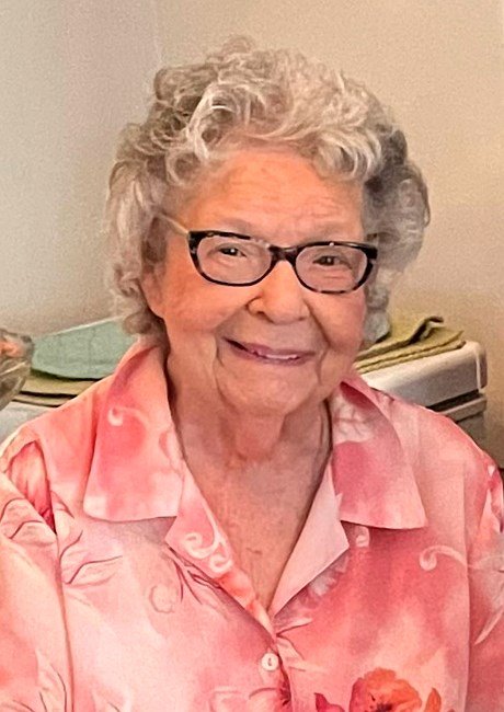 Smiling elderly woman in glasses and pink shirt.