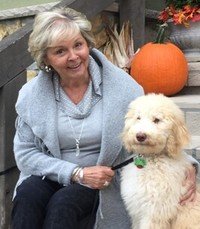 Woman with dog near pumpkin and corn decoration.