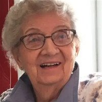 Elderly woman smiling, wearing glasses and a sweater.